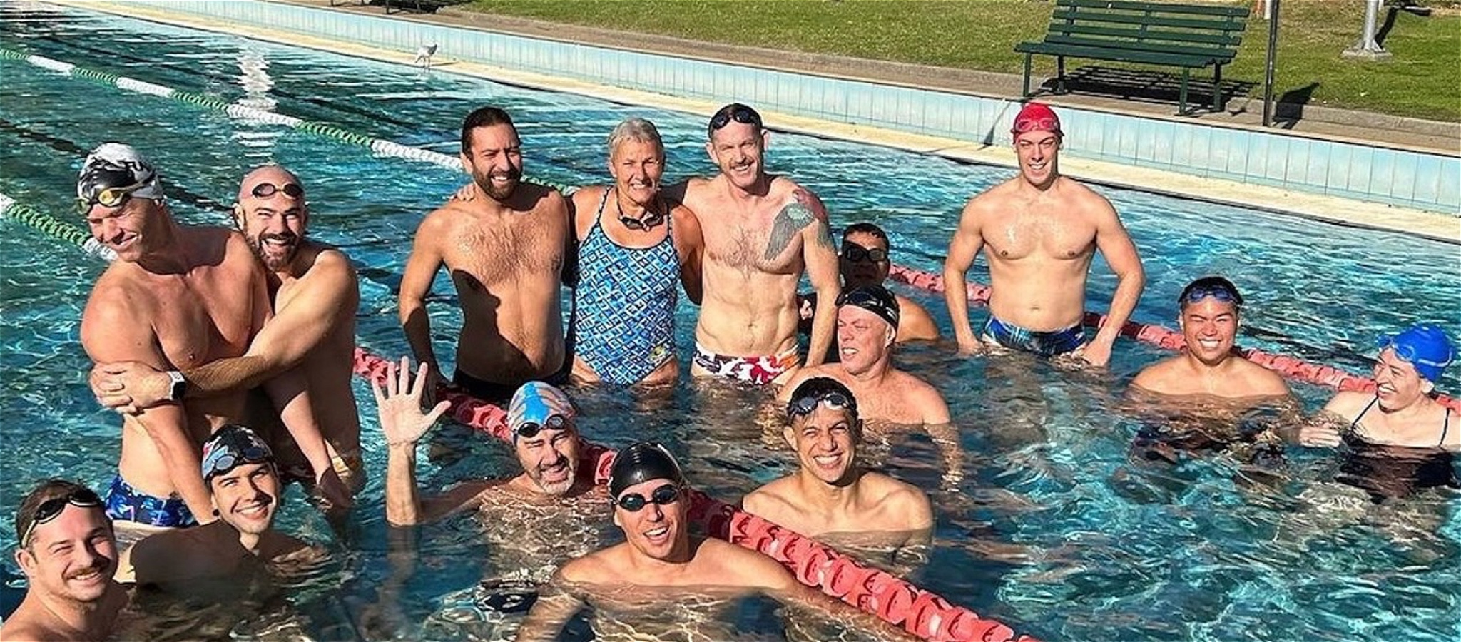 A group of swimmers standing in an outdoor pool, smiling at the camera