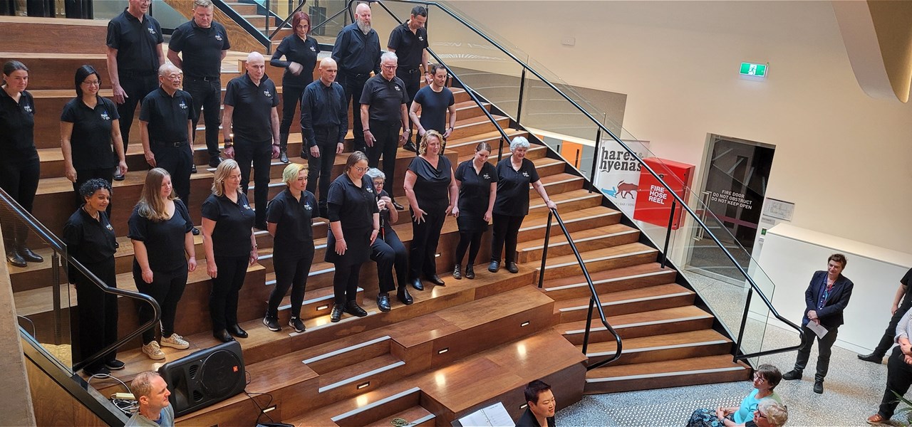 Choir wearing black clothes performing on steps of staircase at Victorian Pride Centre
