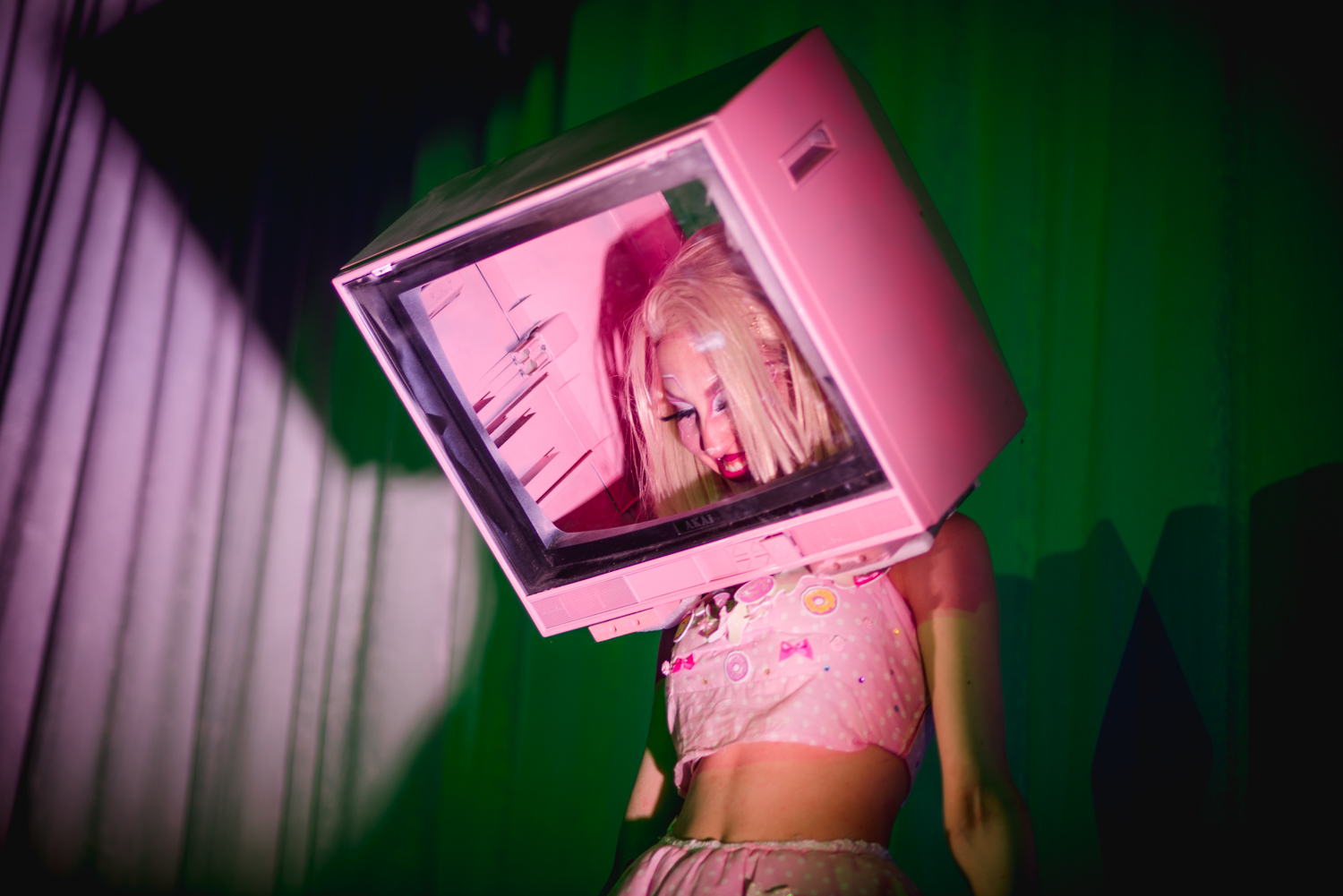 Person scantily dressed in pink, with their head inside a pink analogue TV
