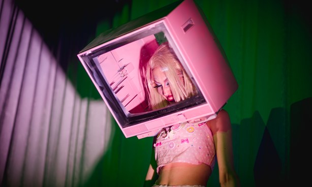 Person scantily dressed in pink, with their head inside a pink analogue TV