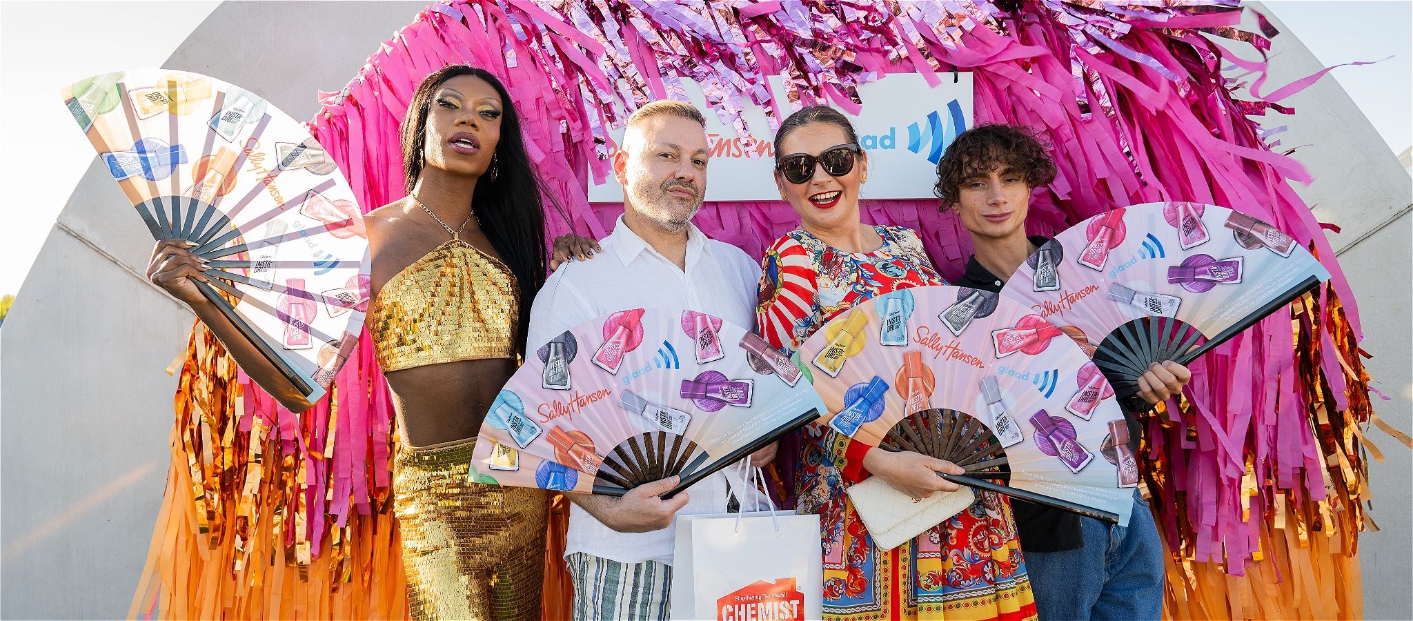 4 people holding fans in front of a wall of tinsel
