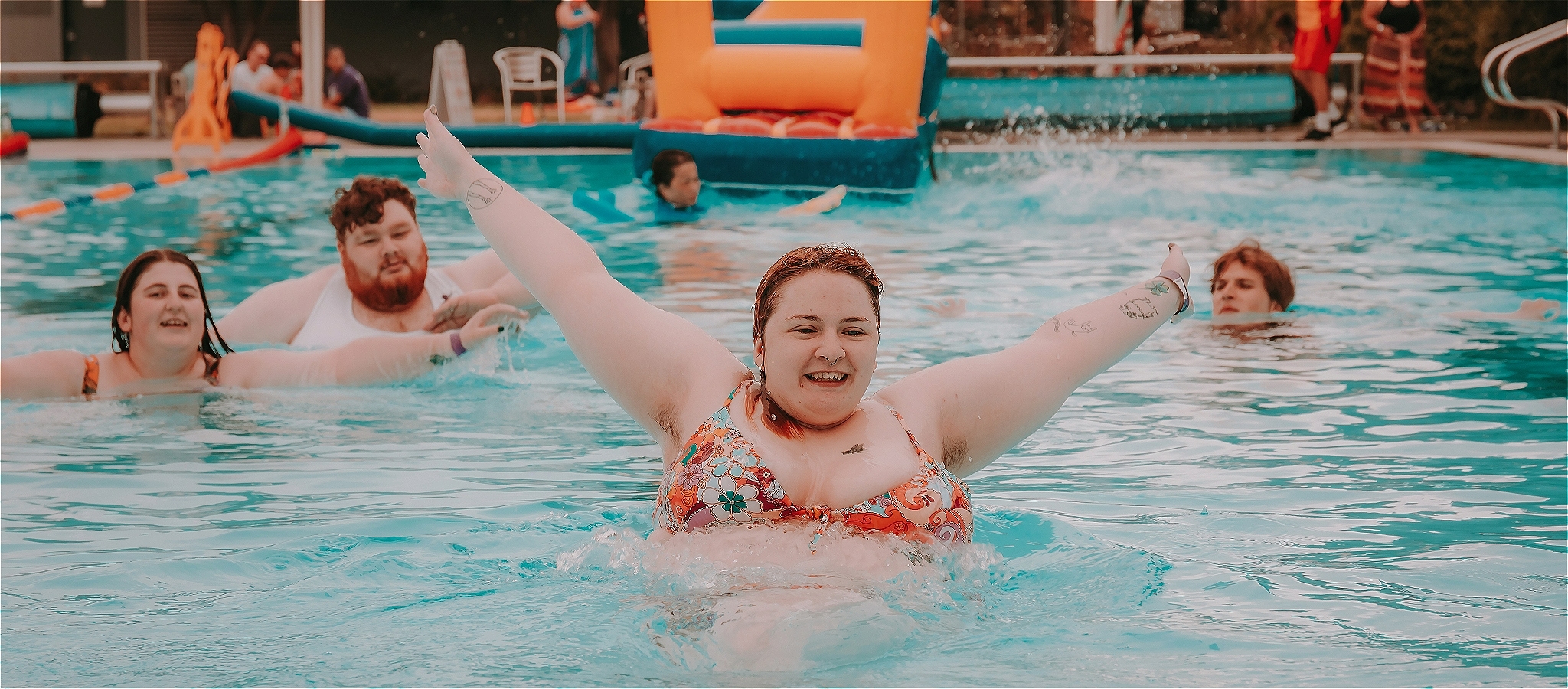 Several young people having fun in the pool at the Pride Pool Party in Sunshine event last year. One of them is leaping out of the water with a smile