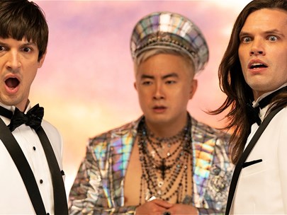 Two people wearing white suits facing each other stare towards the camera with shocked faces. Between them is a person dressed in silver.