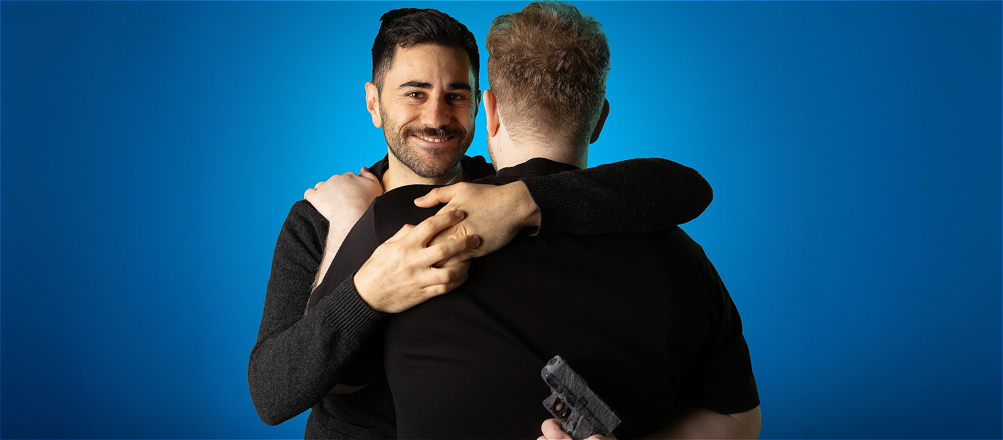 Two men embracing, one with their back to the camera. The other is smiling broadly.