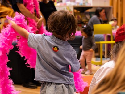 A group of young children in a library. Some are holding long, pink feather boas.