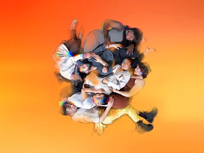 Image description: A photograph taken from above of a group of seven people of diverse ages, body types, skin tones, and clothing cradling one another on a background of dark to light orange featuring pencil-drawn outlines of their bodies and four faded rainbow-coloured outlines of their bodies and four rainbow coloured rectangles layered across some of the forms.