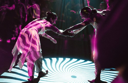 Who people holding hands and dancing around a circular pattern on stage