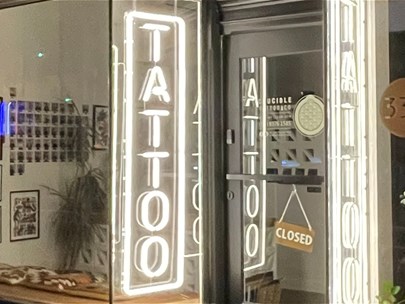 Exterior photo of a tattoo studio, with bright fluorescent lights that read 
