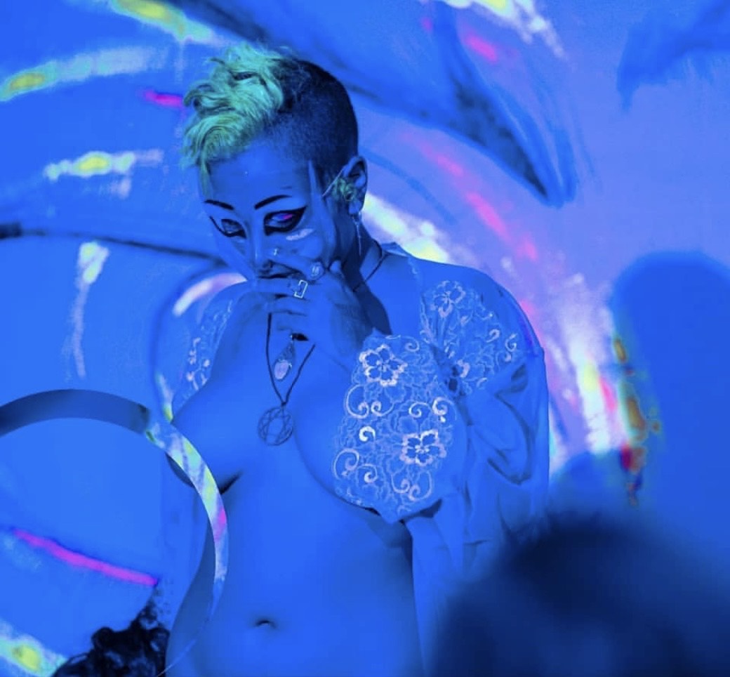 Plastic Messiah with boobs bared under blue lighting