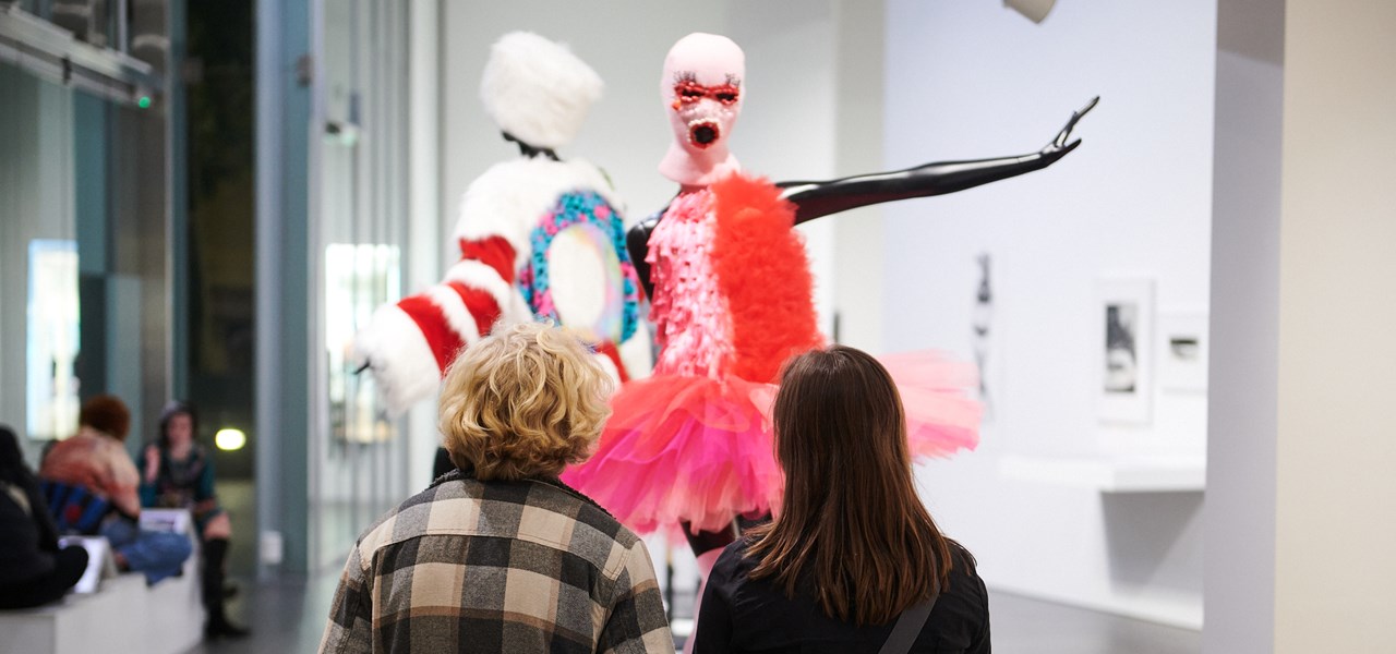 Visitors viewing an exhibit at the NGV. The exhibit is a mannequin in a red chiffon dress with a red boa.