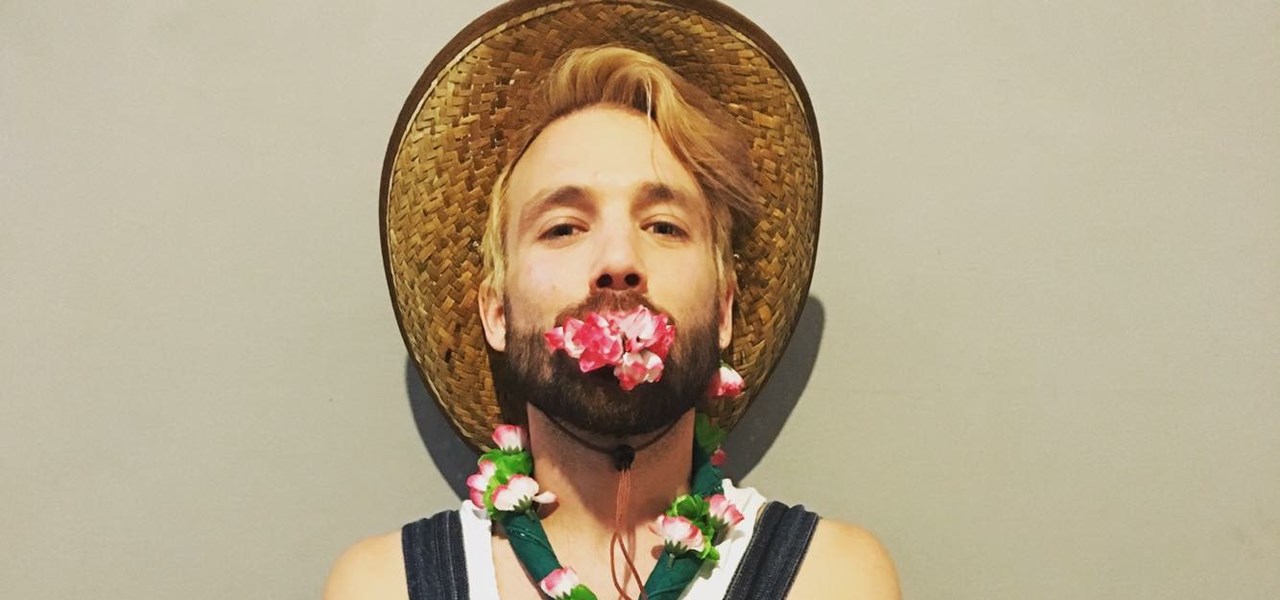 Portrait of Matt wearing overalls, a straw hat, a mouthful of flowers and more flowers decorating the overalls