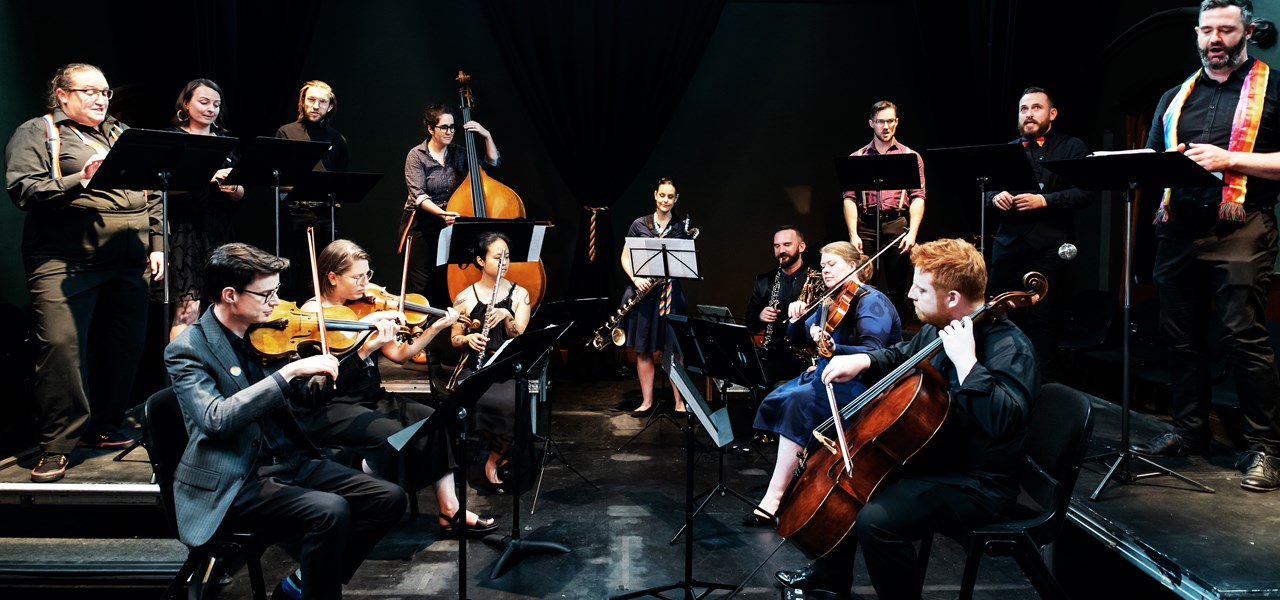 A large chamber orchestra playing against a black background, with everybody dressed in black