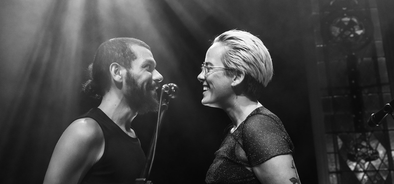 Black and white image of two people on stage, facing each other, very close to each other