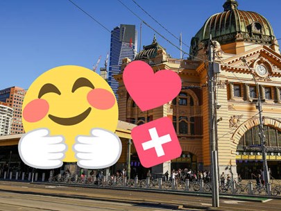 Image of Flinders St Station with 3 stickers - a yellow smiling face - a pink heart - and a white cross on a red background