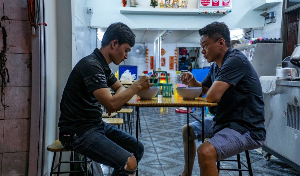 Two Asian males dining at a table with a kitchen in the background