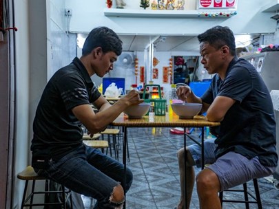 Two Asian males dining at a table with a kitchen in the background
