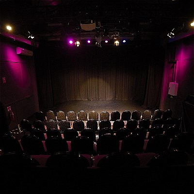 Dark performance space with empty seats in the foreground and a spotlight on an empty stage