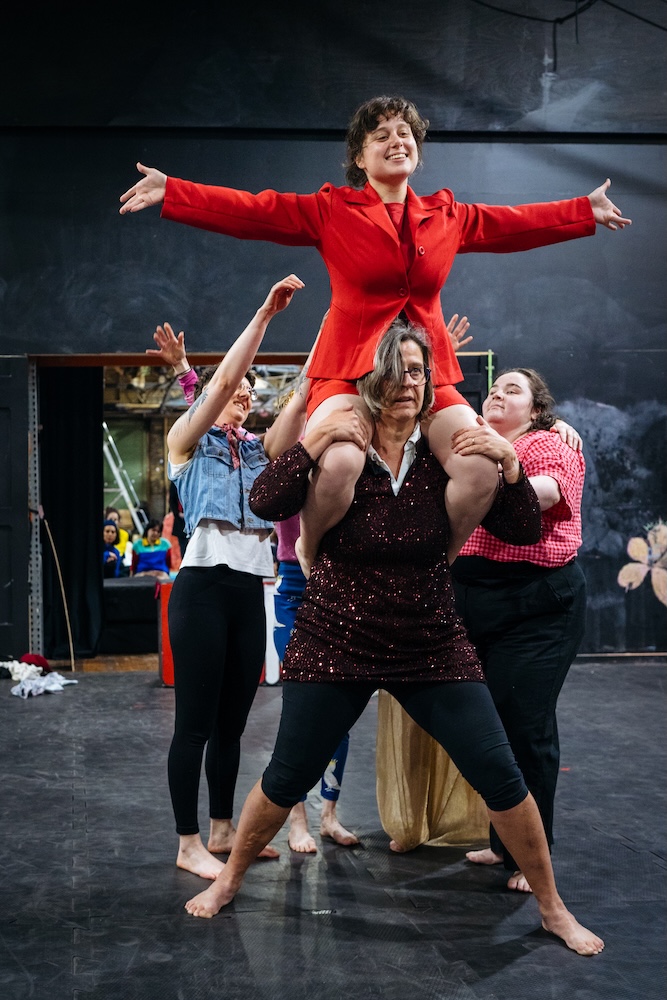 Members of the Women's circus. One is holding another on their shoulders while others stand ready to assist.