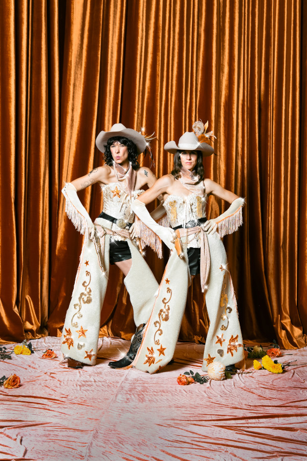Two people standing in front of a gold curtain wearing a gilded cowboy outfit