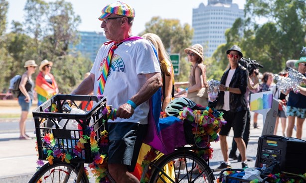 A man on a bicycle at Midsumma Pride March - the bicycle and the man are adorned in rainbow acoutrement
