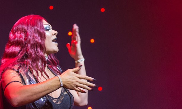 Person singing, one arm in front, the other vertical in front of their face. Slight red hues, with stars behind