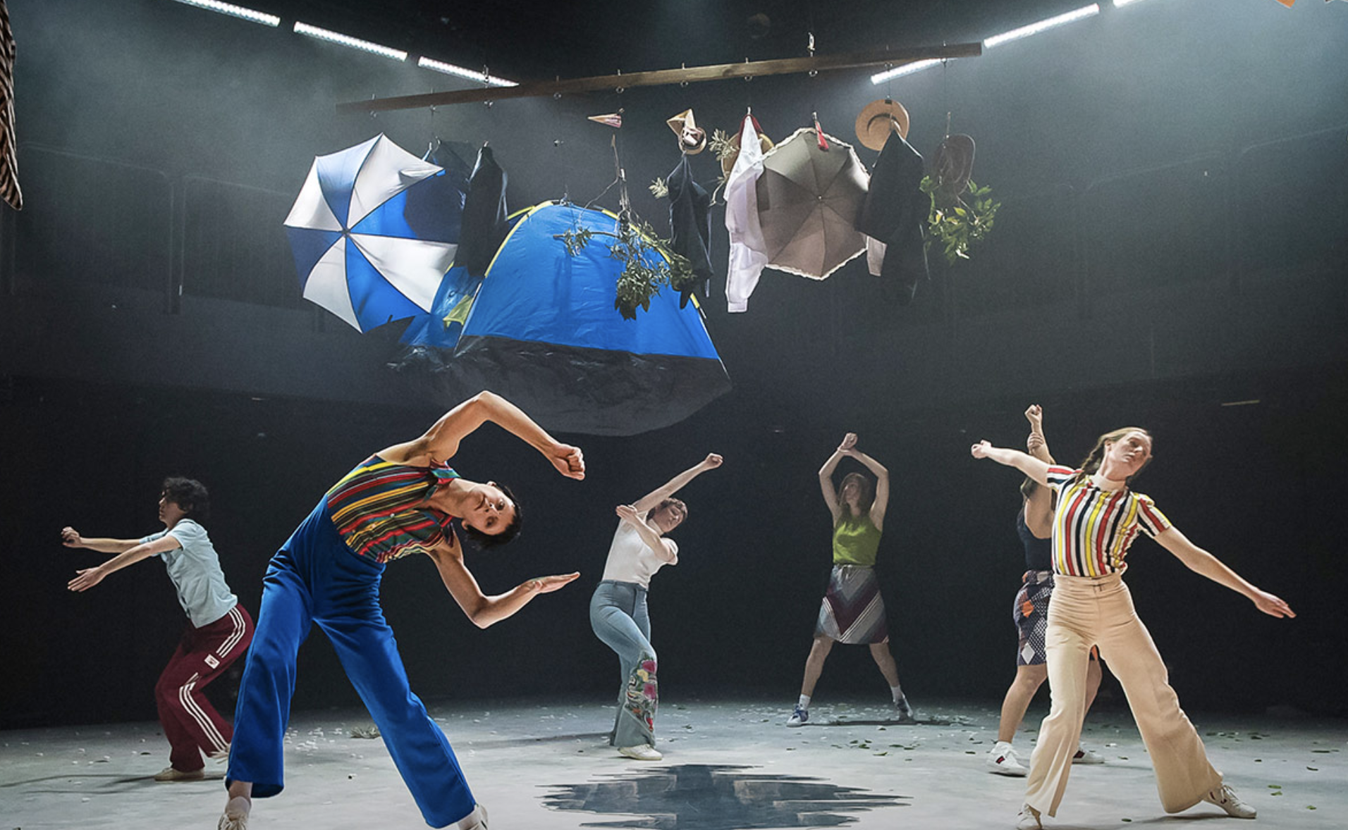 Dancers on stage bending sideways, large umbrellas and other objects hanging above them