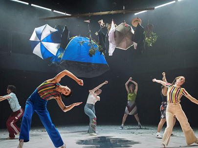 Dancers on stage bending sideways, large umbrellas and other objects hanging above them