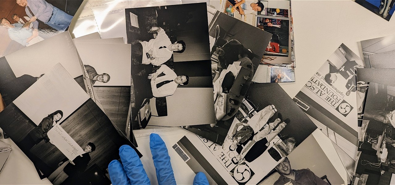 A person wearing blue gloves examines archival photographs.