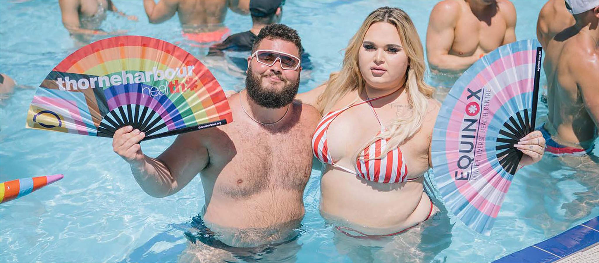 Two friends fanning themselves as they stand together in a swimming pool.
