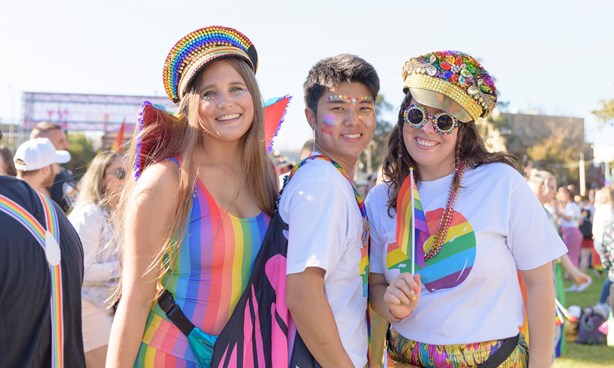 Three people dressed in rainbow colours in a park setting