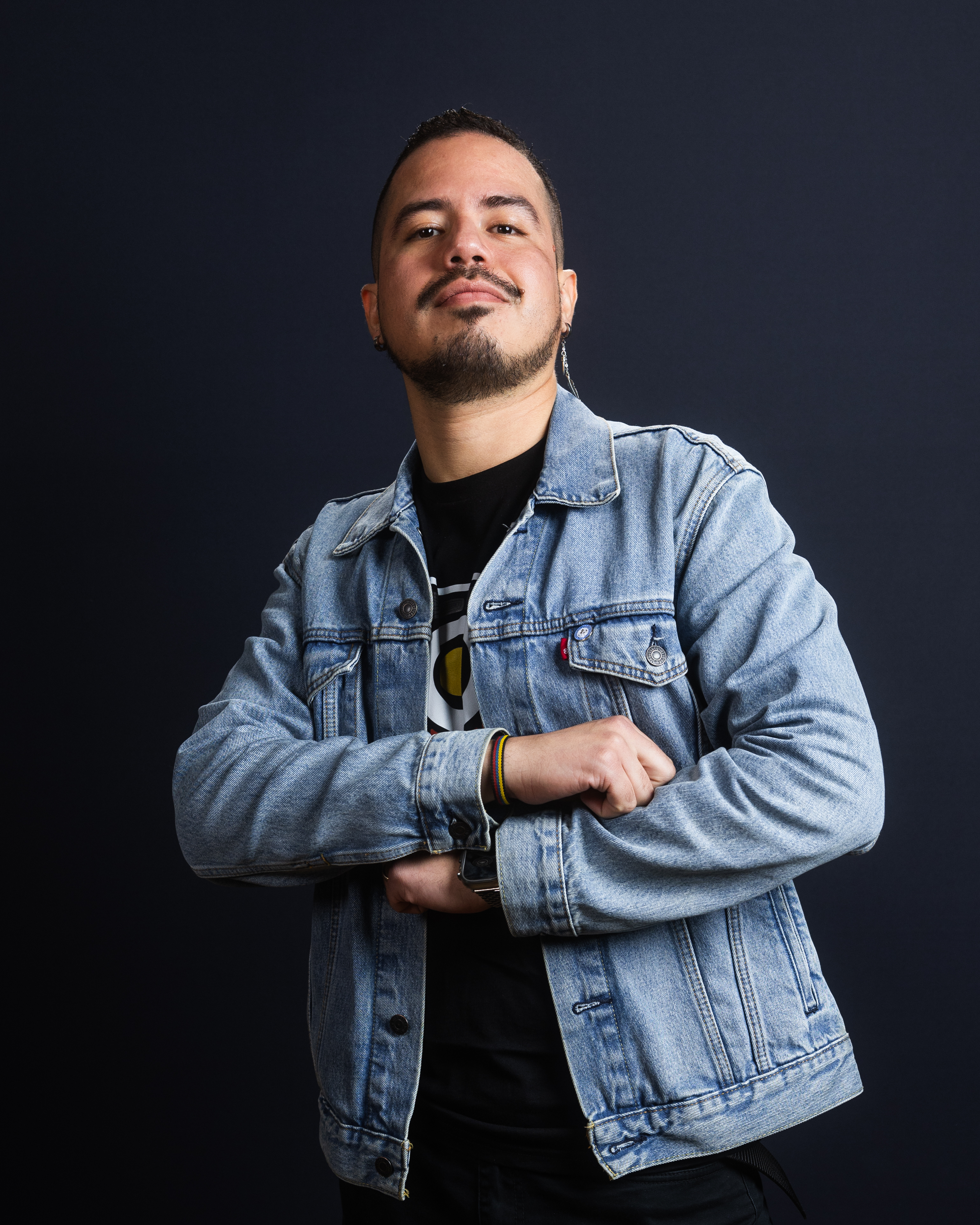 Jase Lasso with arms folded wearing a denim jacket - against a black background