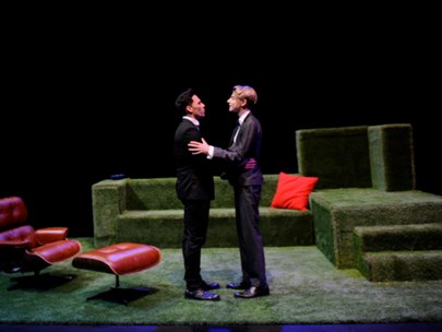 Two men standing on a stage facing each other, with arms around each other (but a small distance between them)