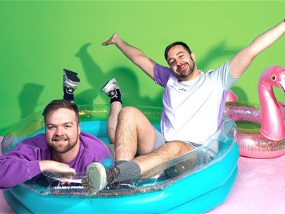 Two people looking happy, sitting in a plastic pool with a pink plastic swan-shaped lilo behind them