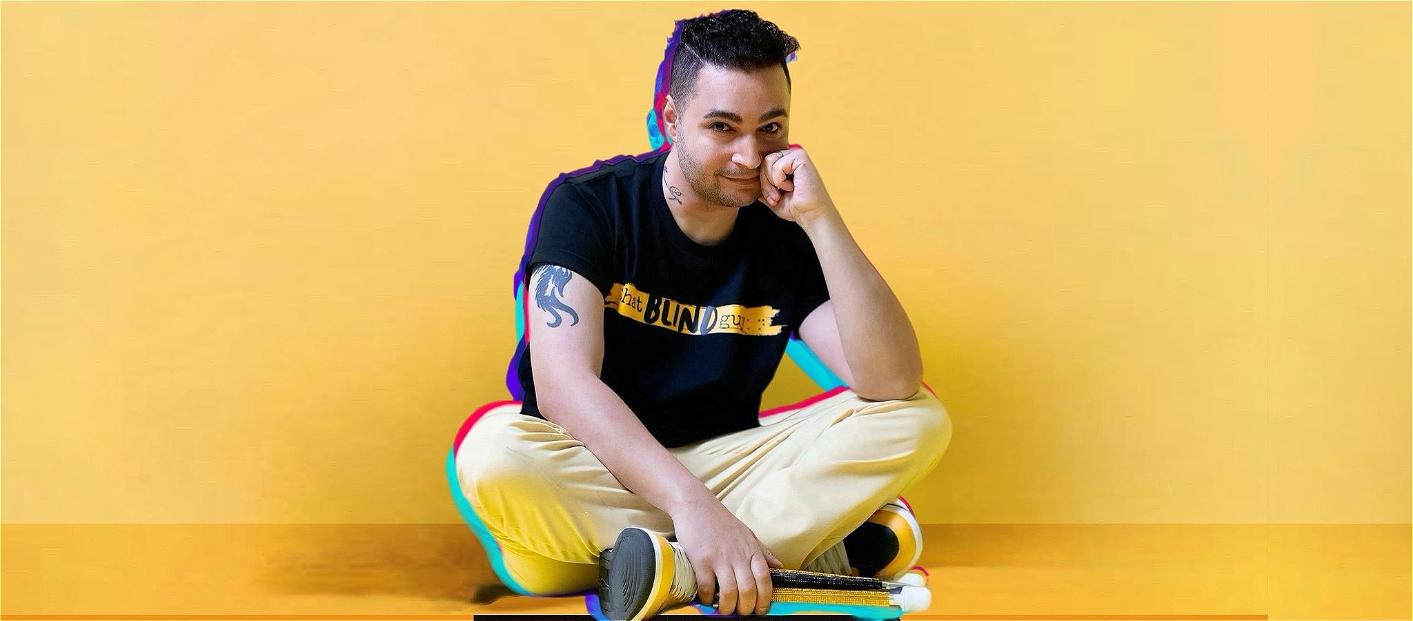 Karan Nagrani wears a black t shirt and brown trousers. He sits crossed legged on the floor and looks pensive