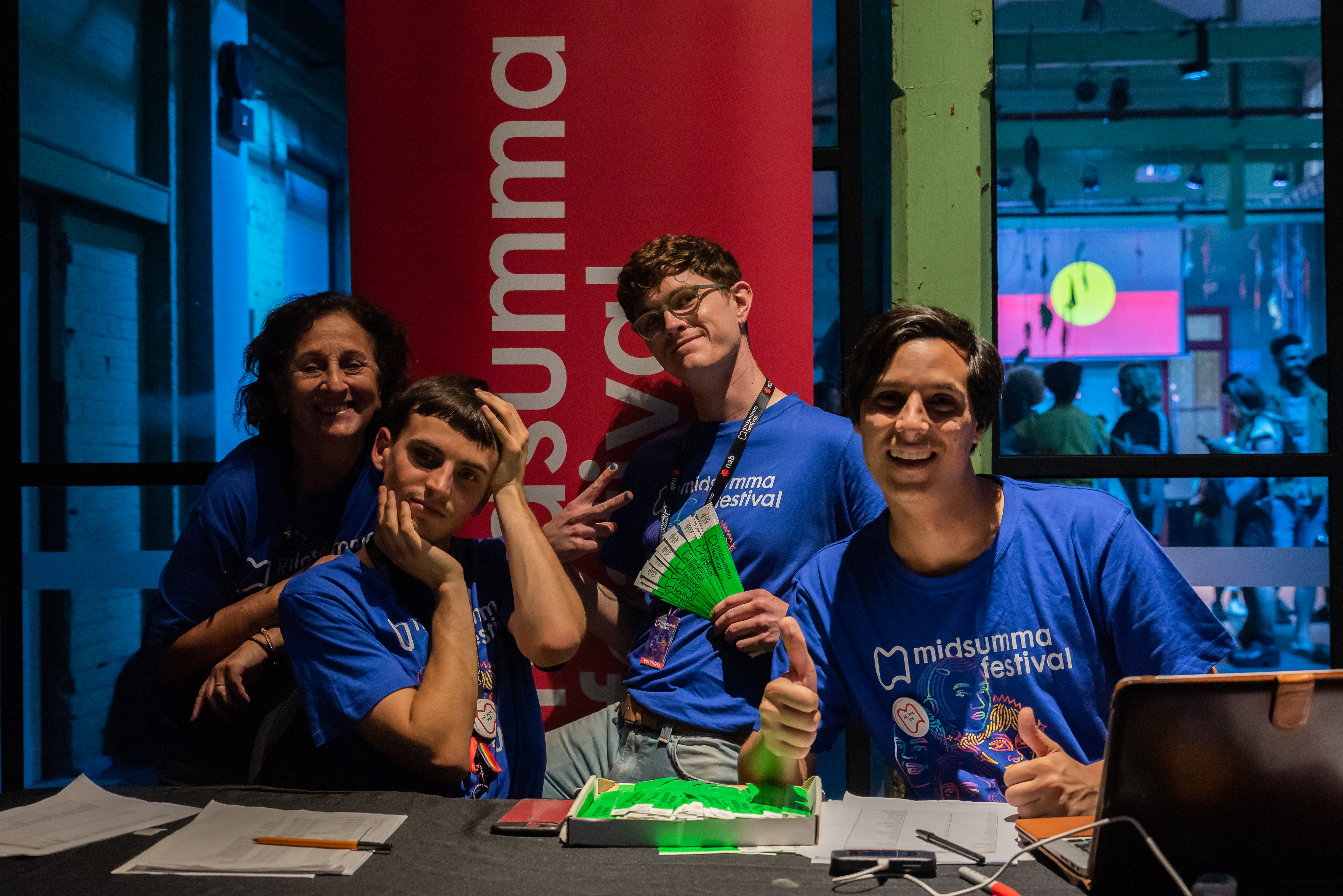 Four happy Midsumma volunteers sitting at a box office desk in a venue
