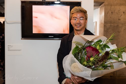Jack Lee holding flowers, standing in front of their submission
