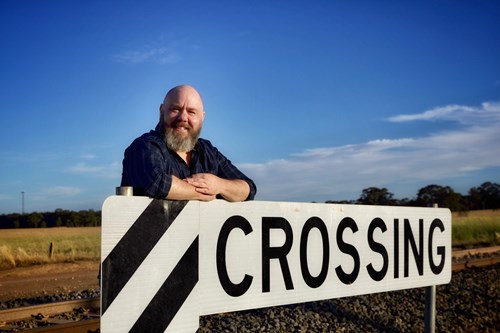 Bearded person leaning on a railway crossing sign