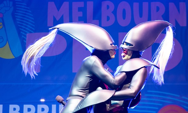Two figures embracing while dressed in silver "space costumes" - sleek full body outfit + helmet with a hair ponytail coming out of the helmet