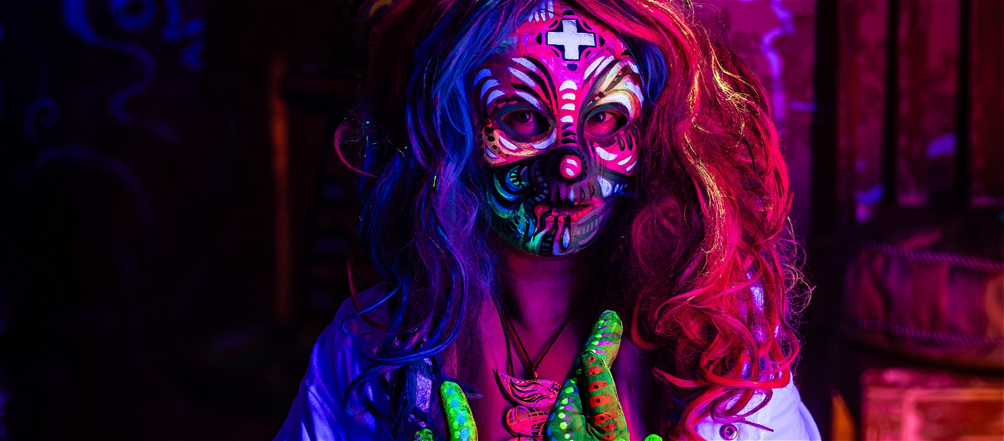 A person wearing a colourful mask and outfit lit with neon lights to make it glow.