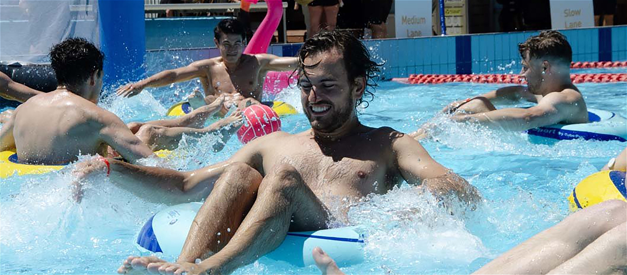People sitting on inflatable donuts playing "Bumper Polo" and splashing around the pool.