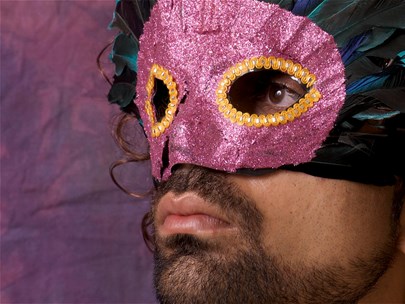 Headshot of a person with thick brown hair wearing a pink mask. The mask has feathers above it to hide the top of their head