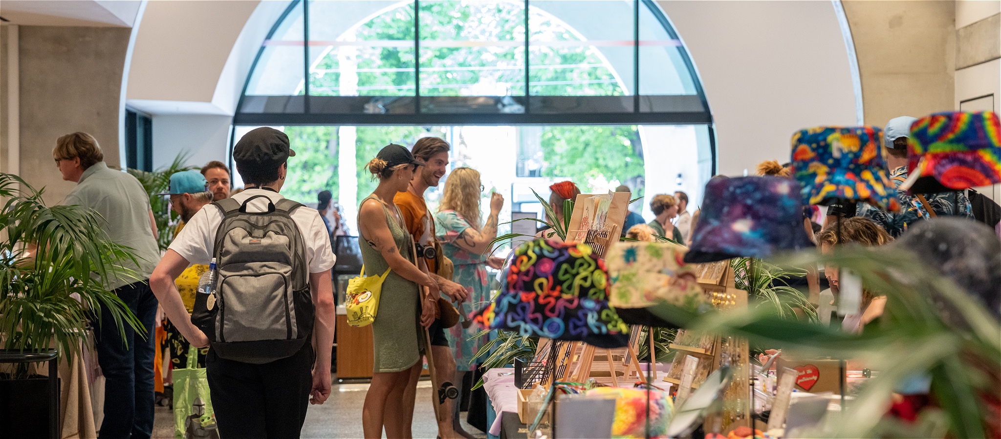 A crowd wanders through the lively Gay Stuff Market stalls inside the Victorian Pride Centre, browsing colourful rainbow merchandise from queer makers