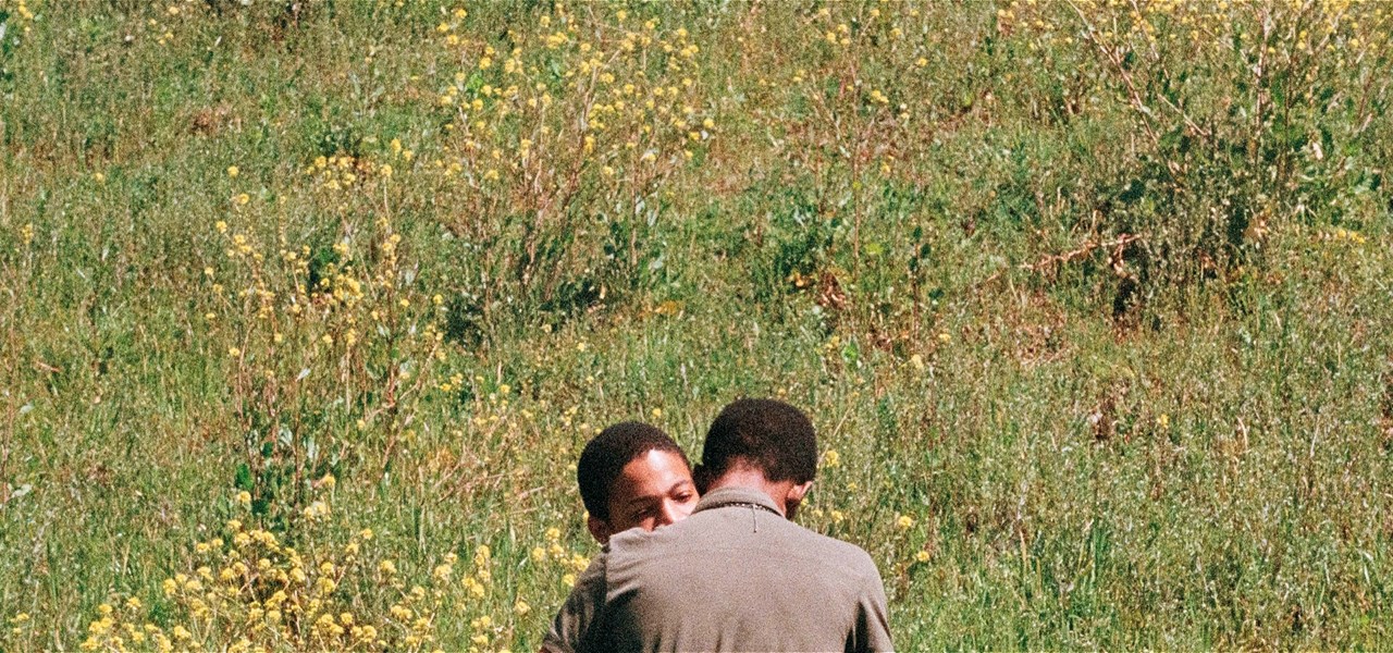 Two men embracing in a sunny field.