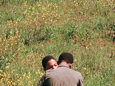Two men embracing in a sunny field.