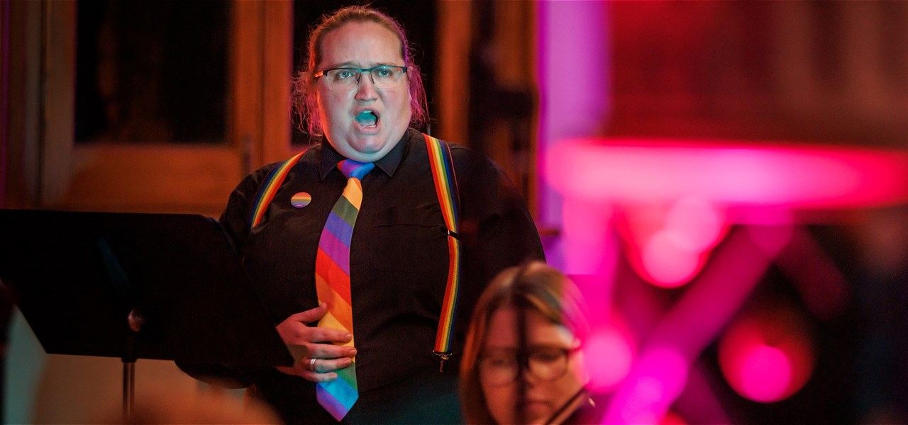 A singer in black clothes and a rainbow tie sings with a very intense expression