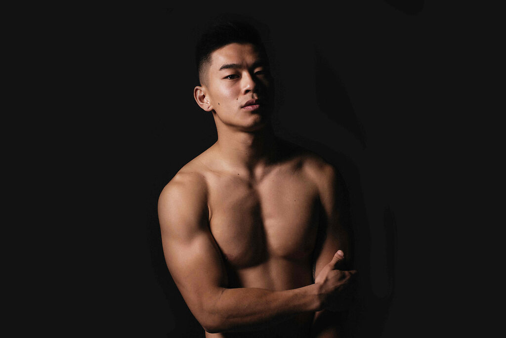 Bare-chested Asian male against a black background