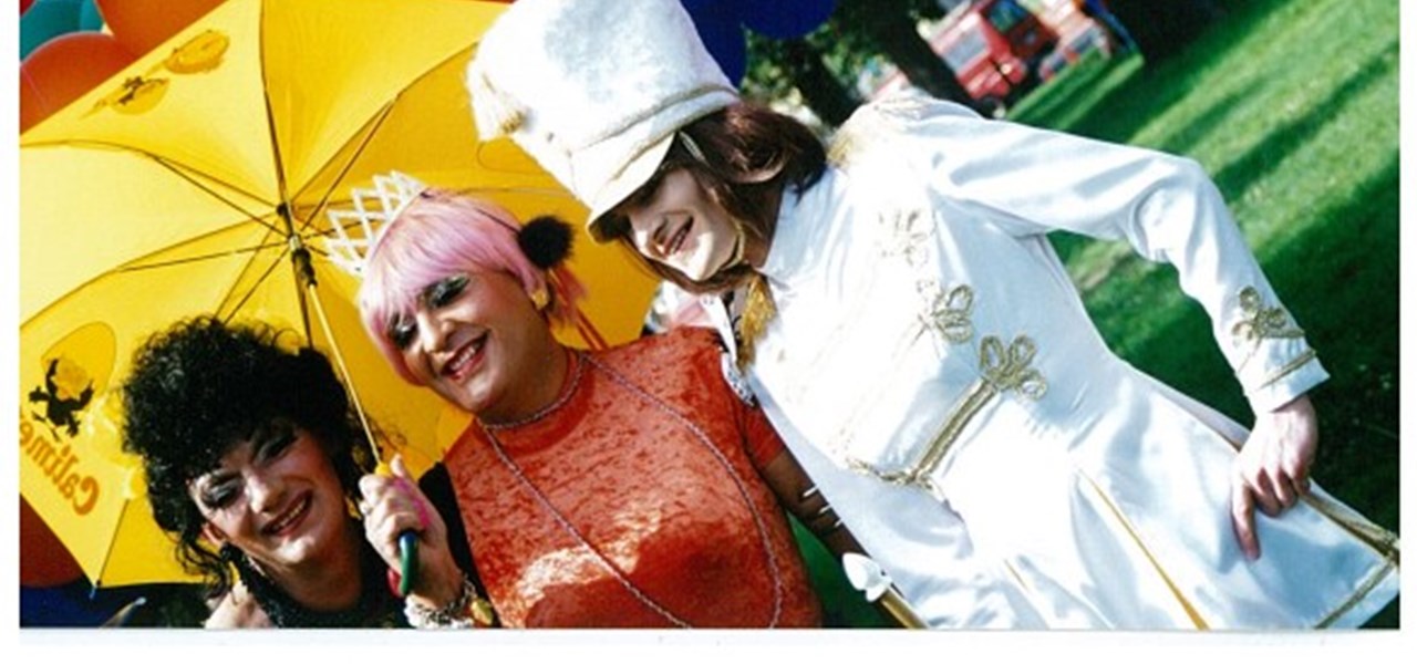 Pride March 2000 image: a happy looking trio of lesbian-looking people; yellow umbrella; red and blue balloons