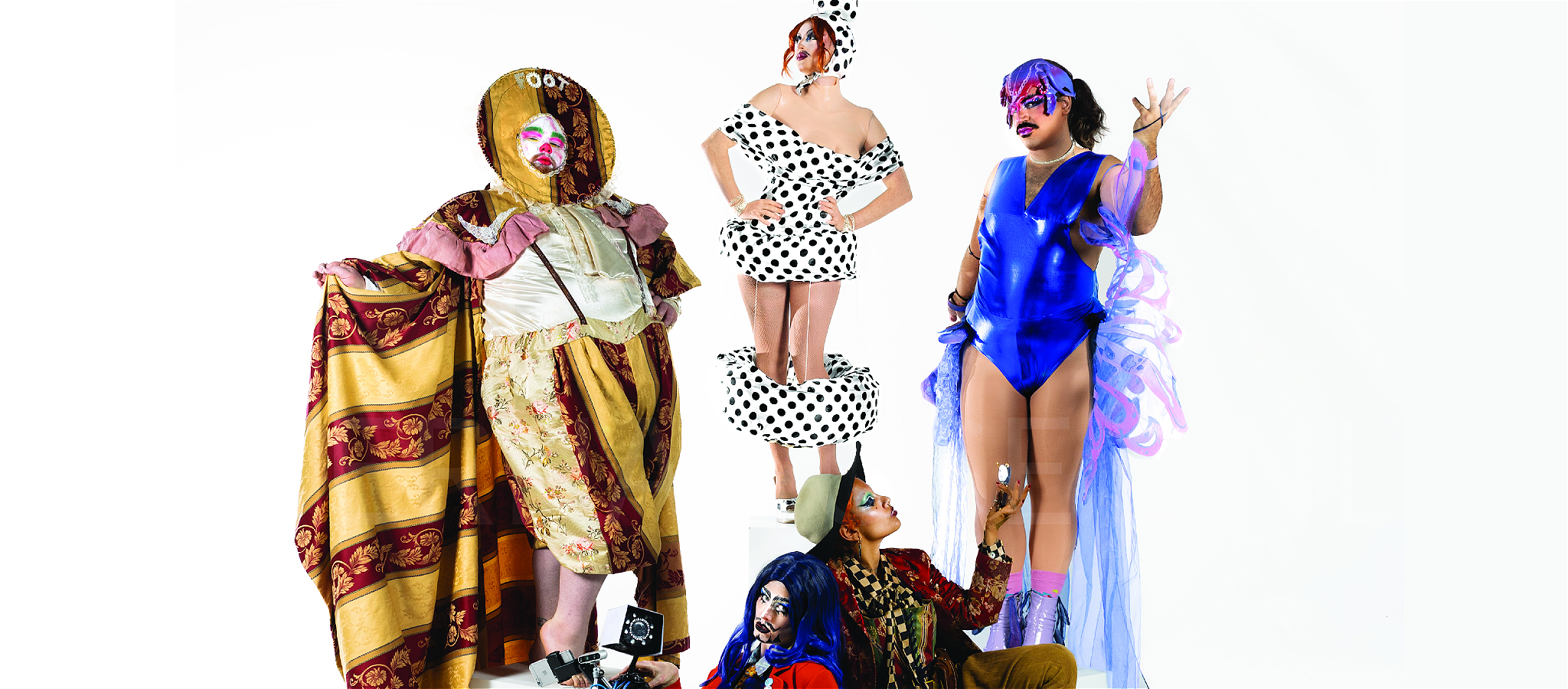 Five performers in eccentric patterned costumes standing on plinths against a white background.
