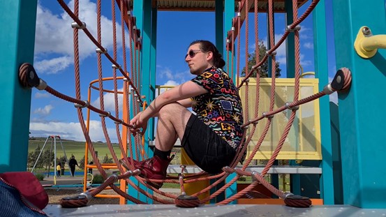 Gabriel sitting amongst some ropes in a playground setting