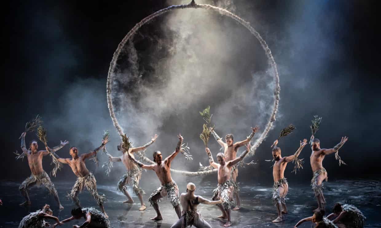 Indigenous dancers around a large hoop, which seemingly represents a full moon. Smoke give the illusion of clouds